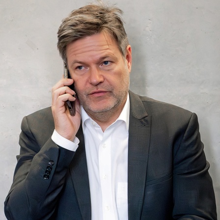 Robert Habeck, Bundeswirtschafts- und Klimaminister (Die Grünen), lehnt an einer Wand und telefoniert.