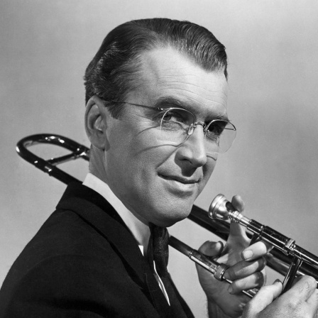 Der Musiker Glenn Miller schaut euf einem schwarz-weiß Foto in die Kamera und hält dabei seine Posaune in den Händen.