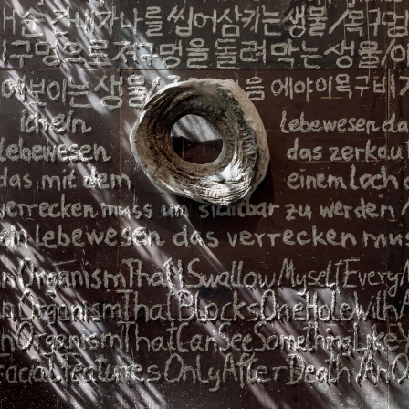 Blick in die Ausstellung im MMK: Ein auf die Wand mit einem in Flüssigbeton getauchten Zeigefinger geschriebenes Gedicht auf Deutsch, Englisch und Koreanisch.