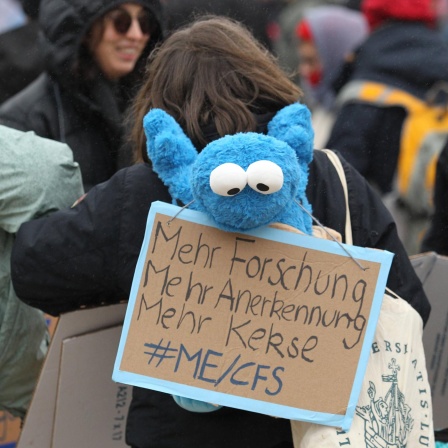 Eine Demonstrantin fordert auf einem Plakat mehr Forschung und mehr Anerkennung für ME/CFS.