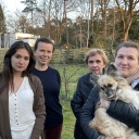 Das Bild zeigt vier Frauen, die auf einer Wiese stehen. Eine hält einen kleinen Hund auf dem Arm.