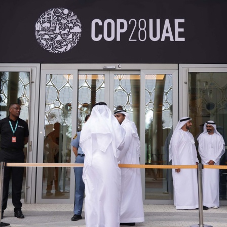 Menschen vor dem Eingang zu einem Konferenzgebäude mit dem Logo der COP28 (29.11.2023).