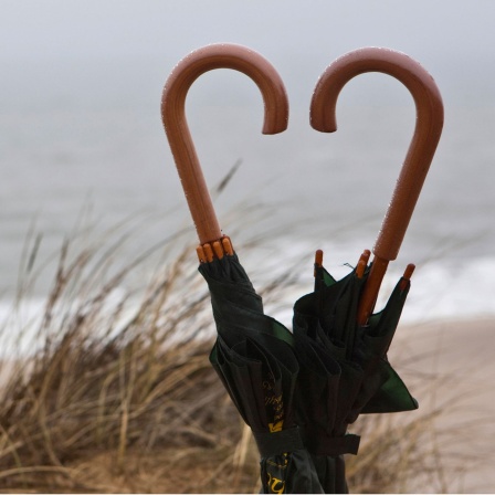 Regenschirme nebeneinander bilden Herz aus ihren Griffen, Strand Nordsee, Sylt.