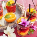 Bunte Cocktails auf Tablett mit Blüten und aufgeschnittenen Orangenhälften