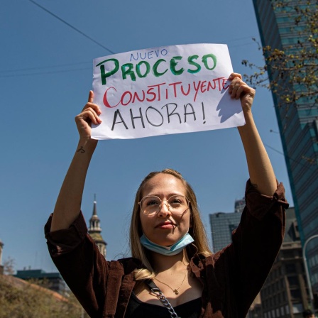 Eine junge Frau trägt während eines Protests ein Schild, das eine neue Verfassung fordert.