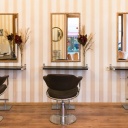 Innenansicht eines Friseursalons: drei Friseurstühle vor drei Spiegeln