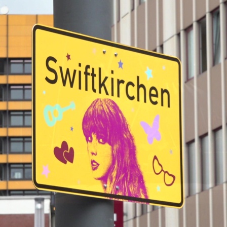 Ein gelbes Schild mit der Aufschrift "Swiftkirchen" und einem pinken Konterfei der Sängerin Taylor Swift hängt in Gelsenkirchen