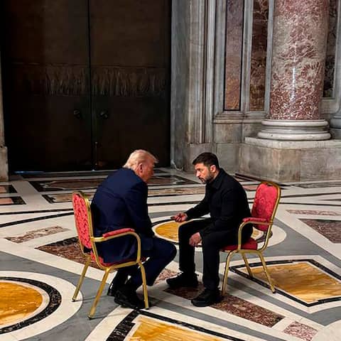 Der ukrainische Präsident Wolodymyr Selenskyj und US-Präsident Donald Trump sitzen sich in einem prunkvollen Raum des Vatikans auf 2 Stühlen gegenüber und unterhalten sich.