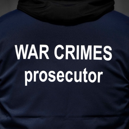 Ein Mann von hinten in einer dunklen Jacke mit der weißen Aufschrift auf dem Rücken "War Crimes prosecutor" 