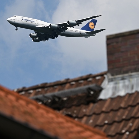 Flugzeug mit Luthansa-Emblem fliegt über Häuser.