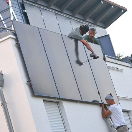 Arbeiter bei der Montage von Solarpanels an der Fassade eines Hauses