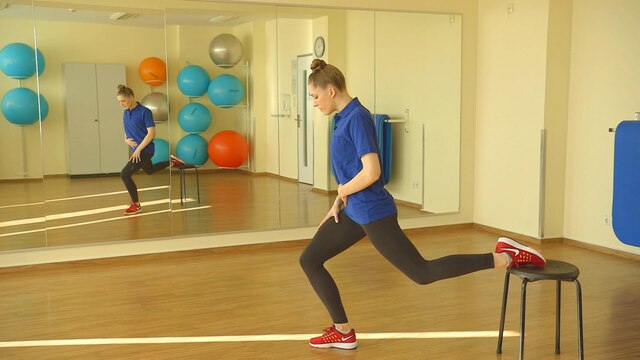 Physiotherapeutin Svea Köhlmoos macht eine Kniebeuge, während sie den anderen Fuß nach hinten auf einen Hocker abgelegt hat.