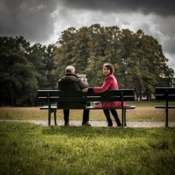 Eine Frau sitzt nehmen einem älteren Menschen auf einer Parkbank.