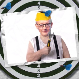 Eine Fotomontage zeigt eine Postkarte auf einer Dartscheibe. Die Postkarte zeigt Friedrich Merz im Unterhemd und mit Hosenträgern. In seiner rechten Hand hält er einen Schraubenschlüssel. Auf dem Kopf trägt er einen gelben Schutzhelm.