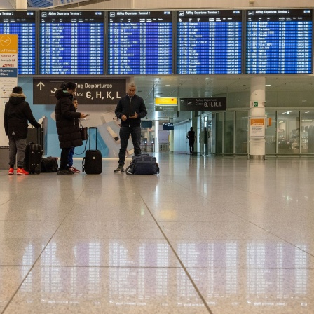 Gestrandete Passagiere stehen am Flughafen München vor einer Anzeigetafel, auf der alle Flüge annuliert sind. 