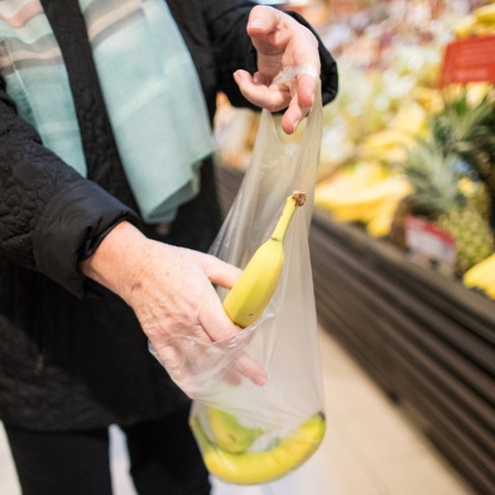 Eine Frau legt Bananen in eine dünne Plastiktüte