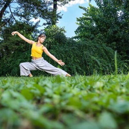 Eine Frau macht Qigong oder Tai-Chi auf einer grünen Wiese.