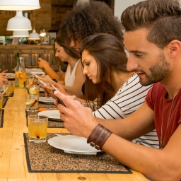 Eine Gruppe junger Leute sitzt an einem langen Tisch und jeder schaut auf sein Smartphone.