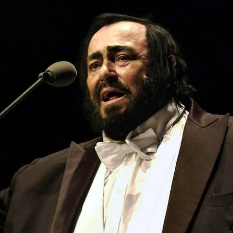 Der Opernsänger Luciano Pavarotti singt vor einem Mikrofon in einem schwarzen Frack.