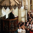 Ein Pfarrer predigt von der Kanzel in einer vollbesetzten Kirche.