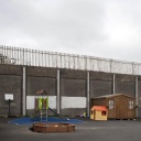 Ein Spielplatz in Belfast, Nordirland, vor einer hohen Mauer, die katholische und protestantische Wohngebiete trennt.