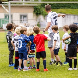 Ein ehrenamtlicher Trainer trainiert Kinder auf dem Fussballplatz.