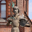Steinfigur eines Ritters mit Schwert und Wappen vor einem Backsteingebäude 