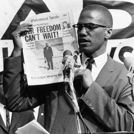 Malcolm X hält bei einer Demonstration 1963 eine Zeitung in die Höhe. Als Schlagzeile steht darauf: "Our freedom can’t wait." - "Unsere Freiheit kann nicht warten."