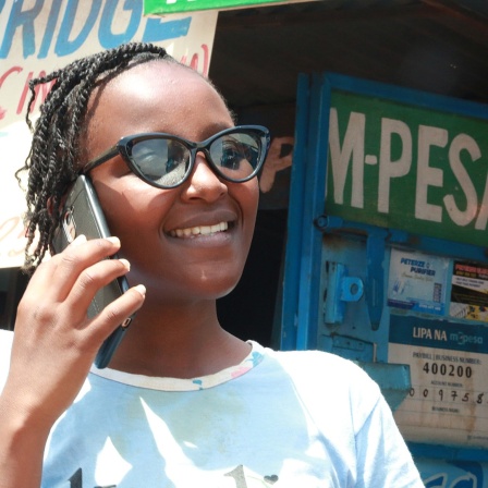 Eine Frau telefoniert mit einem Mobiltelefon in Nairobi, dahinter ein M-PESA Schriftzug.