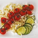 Bandnudeln mit Feta und gegrillten Tomaten und Zucchini auf einem eckigen, weißen Teller