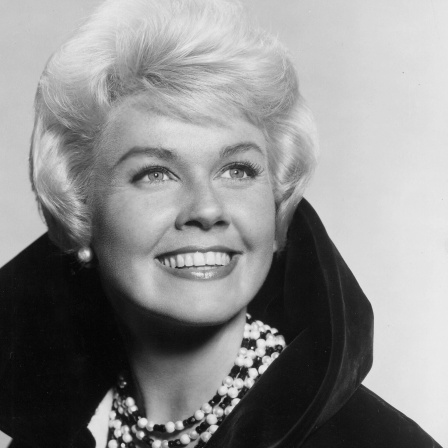 Doris Day: Die Sängerin hat eine blonde Kurzhaarfrisur und trägt einen schwarzen Mantel mit Kragen und eine große Halskette.
