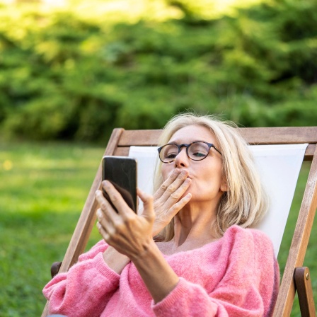 Frau wirft ihrem Smartphone einen Luftkuss zu.