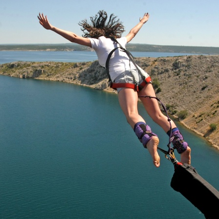 Eine Frau mit ausgebreiteten Armen springt mit Bungee-Seil über der kroatischen Küste von der Brücke Maslenika