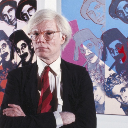Der  US-amerikanische Popkünstler Andy Warhol vor Bilder aus seiner Serie "Ten Portraits of Jews of the Twentieth Century". 1980