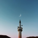 Ein Sichelmond am blauen Himmel hinter einem Minarett.
