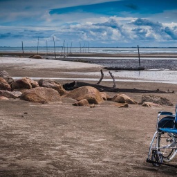 Verliert ein eingeschränktes Leben seinen Wert? Ein blauer Rollstuhl an einem Strand.