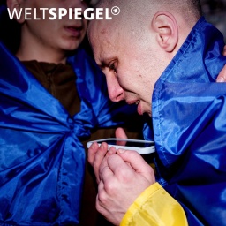 Ein ukrainischer Soldat telefoniert mit einem Verwandten, nachdem er im Rahmen eines Kriegsgefangenenaustauschs in der Ukraine aus der Gefangenschaft zurückgekehrt ist, eine blau-gelbe Ukraine-Flagge um die Schultern.