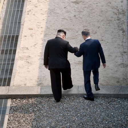 Eine Aufnahme zeigt wie der nordkoreanische Führer Kim Jong Un (L) die Hand des südkoreanischen Präsidenten Moon Jae-in (R) hält, während sie die militärische Demarkationslinie (MDL) überschreiten. Beide trafen sich beim interkoreanischen Gipfel am 27. April 2018 in Panmunjom, Südkorea.