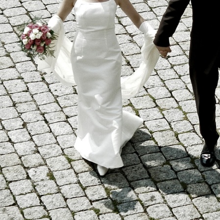 Ein Brautpaar geht Hand in Hand über Kopfsteinpflaster 
