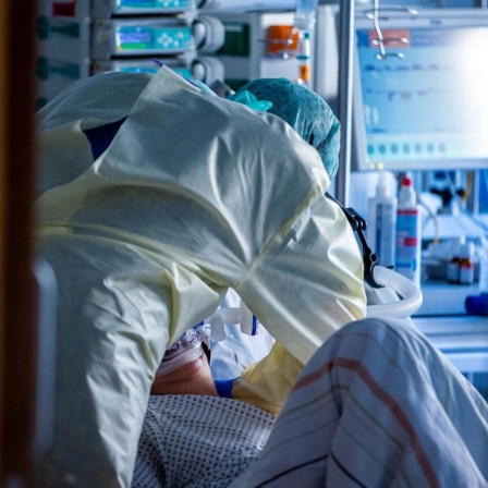 Ein Mitarbeiter richtet bei einer an Covid-19 erkrankten Patientin in einem Zimmer des besonders geschützten Teils der Intensivstation des Universitätsklinikums Greifswald die Beatmungsmaske. 