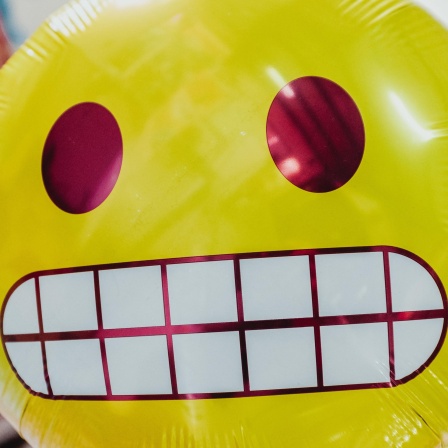 Ein runder gelber Ballon mit einem Emoji-Gesicht, das Zähne zeigt.