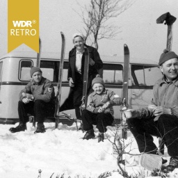 Familie mit Skiern vor Campingbus im Schnee