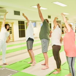 Trainer oder Physiotherapeutin zeigt Senioren eine Stretching-Übung bei der Rückengymnastik.