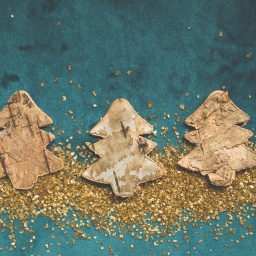 Drei Tannenbäume aus Holz mit goldenem Glitzer auf blauem Hintergrund. 