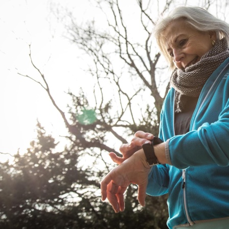 Eine ältere Joggerin in einem Park in Hamburg schaut auf ihr Wearable. (Symbolbild)