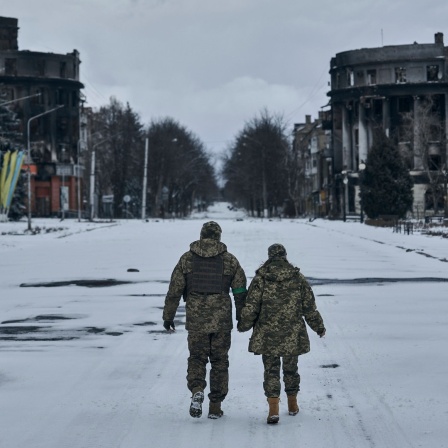 Zwei ukrainische Soldaten, Mann und Frau, gehen in Bachmut Hand in Hand die Straße entlang.
