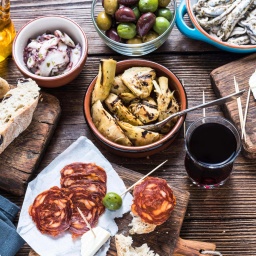 Typische Auswahl an spanischen Tapas, u.a. Salami, Oliven und Sardellen, auf einem Tisch. 