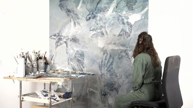 Eine Frau sitzt vor einer Leinwand und malt.