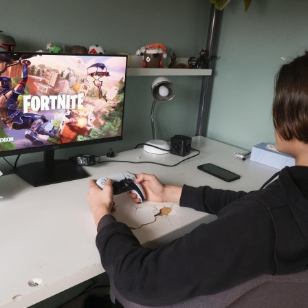 Ein Teeanager sitzt mit Controller in der Hand vor einem Bildschirm und spielt das Computerspiel Fortnite.