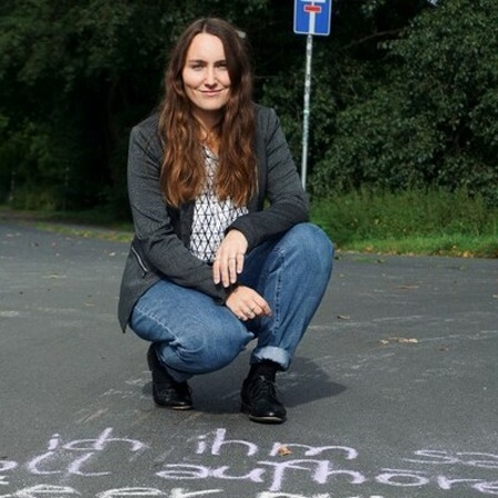Lisanne Richter vor einem mit Kreide geschriebenen Text auf einer Straße.